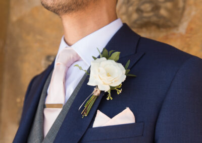 Groom in blue suit with grey waistcoat, blush tie and white rose