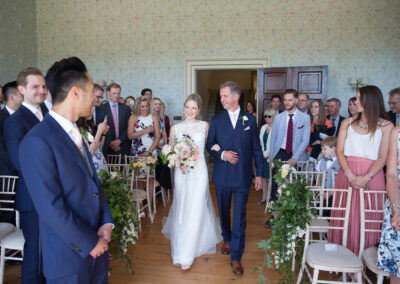 father of the bride walking bride down the aisle at wedding ceremony in drawing room