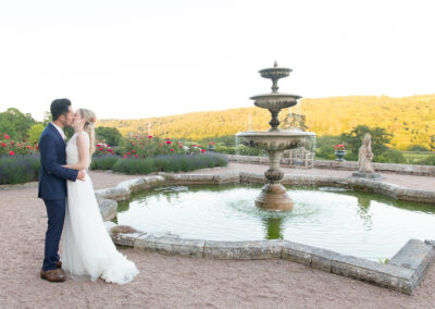 bride and groom kissing by a fountain in the rose gardens at a country house