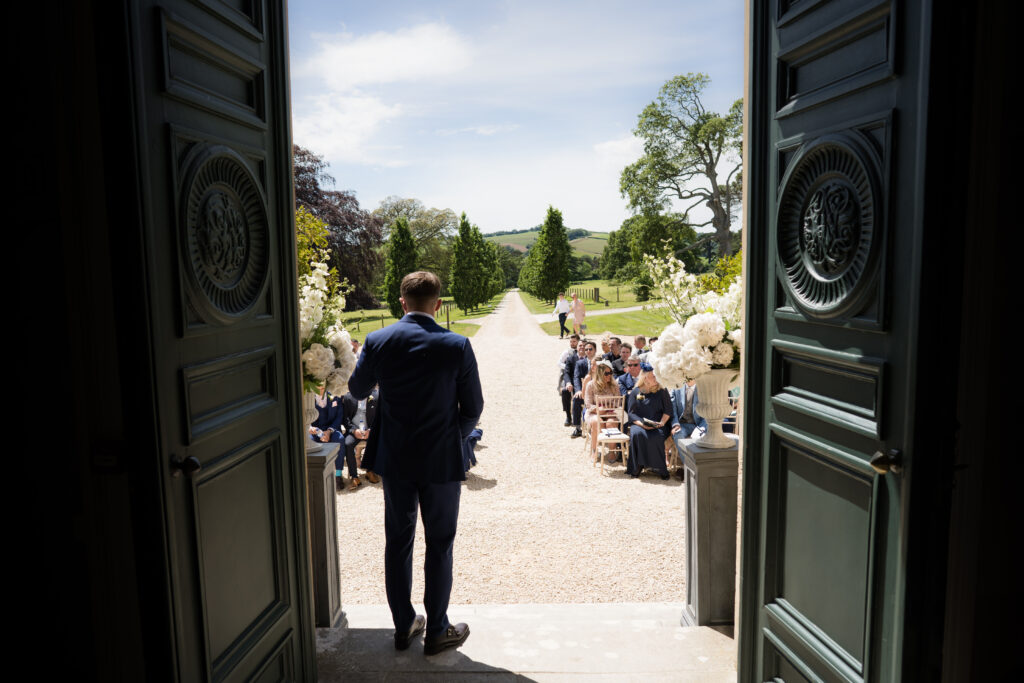 groom looking down the aisle at outdoor ceremony at country house