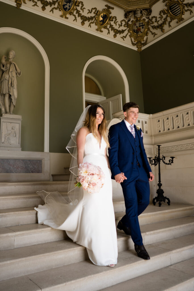 Bride and groom walking down stairway in Entrance Hall