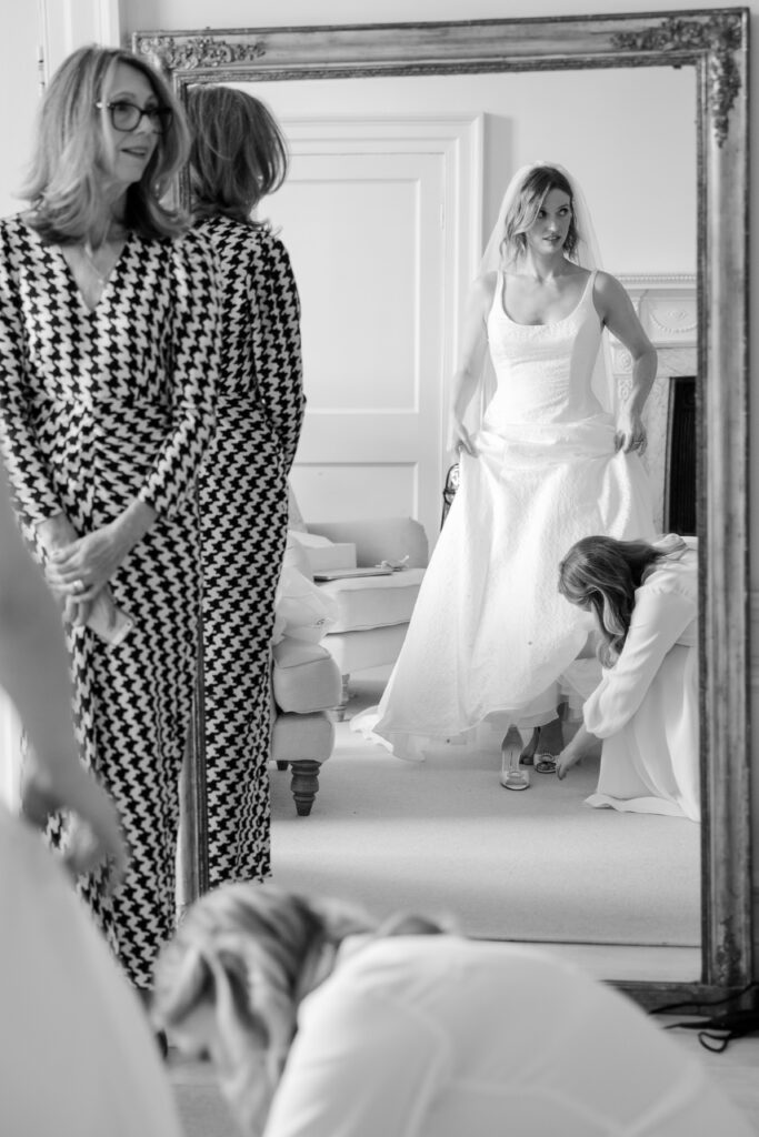 Black and white photo of a bride looking in the mirror, wearing a white wedding dress.
