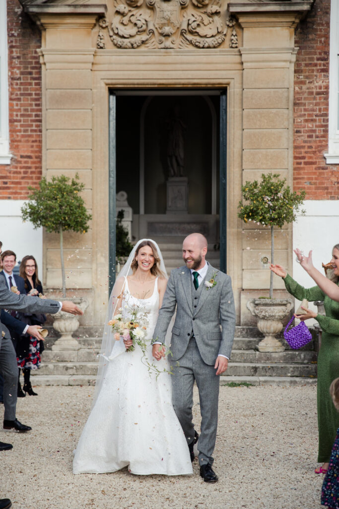 Bride and groom having confetti shot after being married, with English country house behind them.