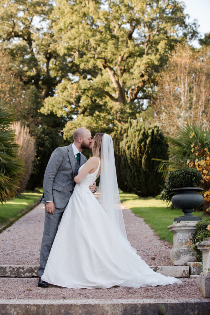 Husband and groom standing on pathway with autumnal trees behind.