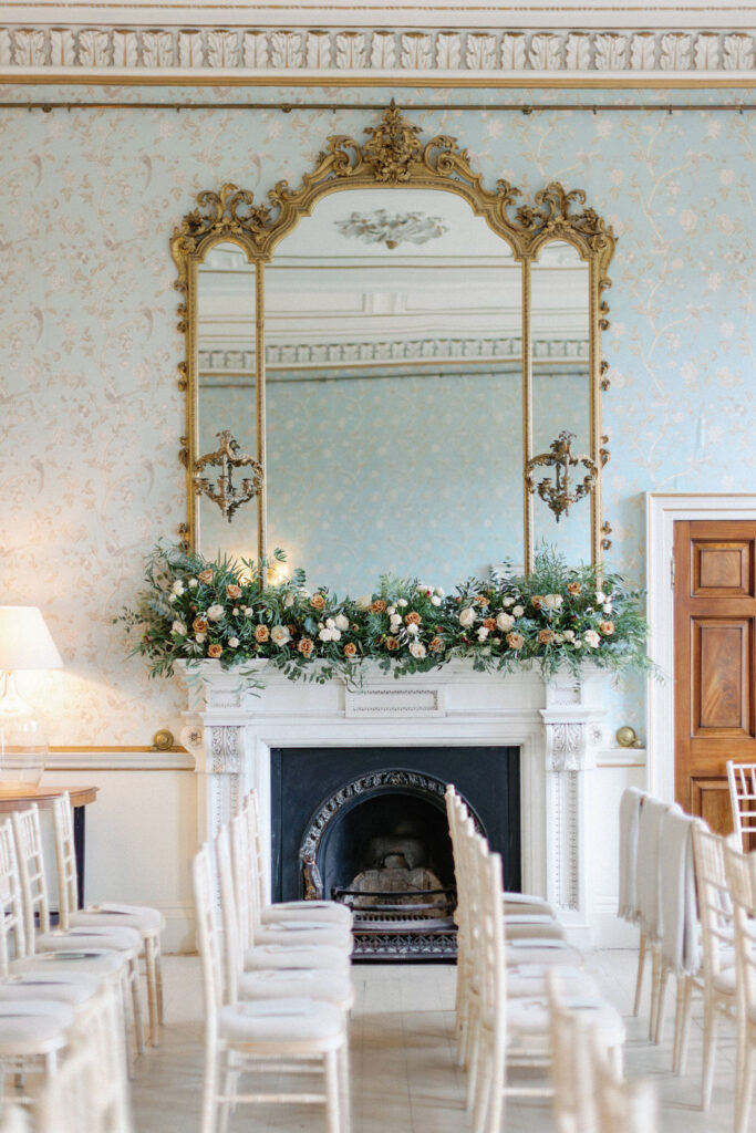 Wedding chairs in Drawing Room with gold mirror and bouquets of flowers behind.