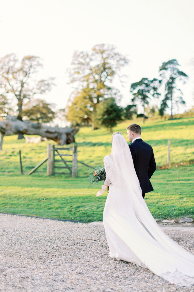 Bride and groom walking down drive, next to Devon field.