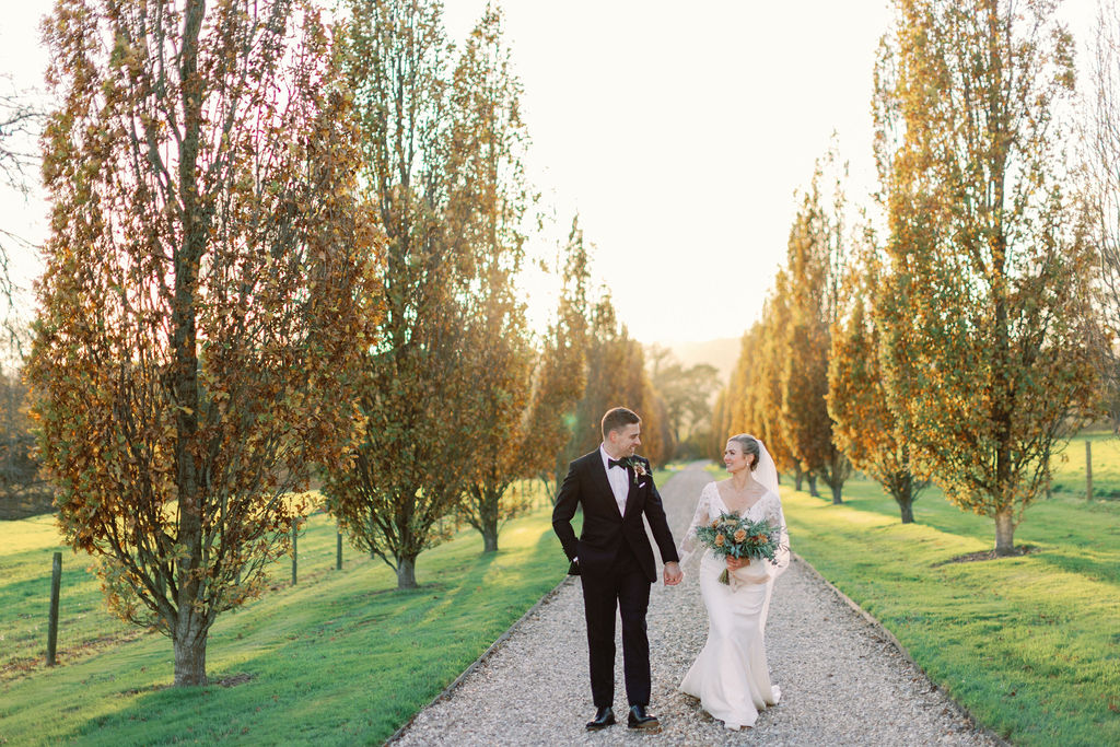 Bride and groom walking down tree lined drive, next to Devon fields.