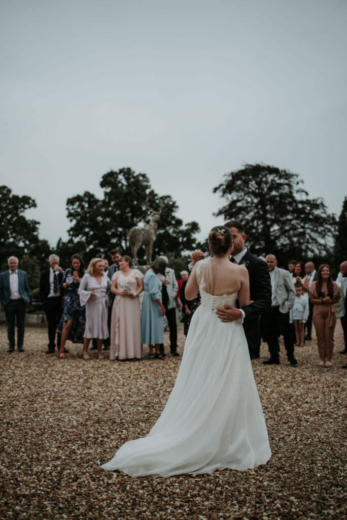 Bride and groom doing first dance in courtyard, surrounded by guests.