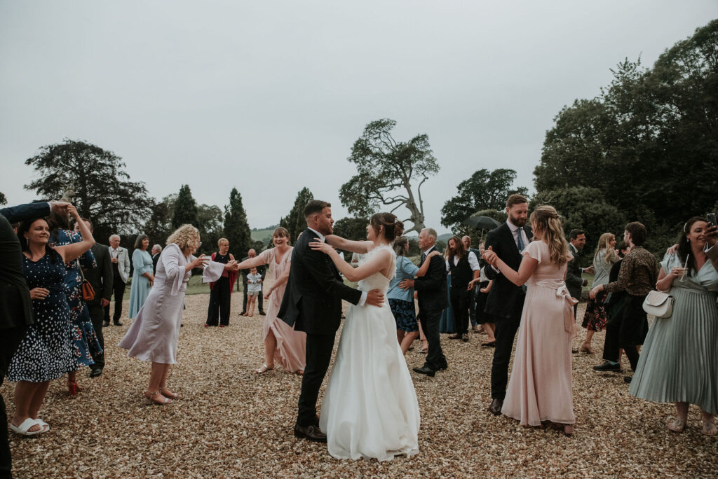 Bride and groom doing first dance in courtyard, surrounded by guests.