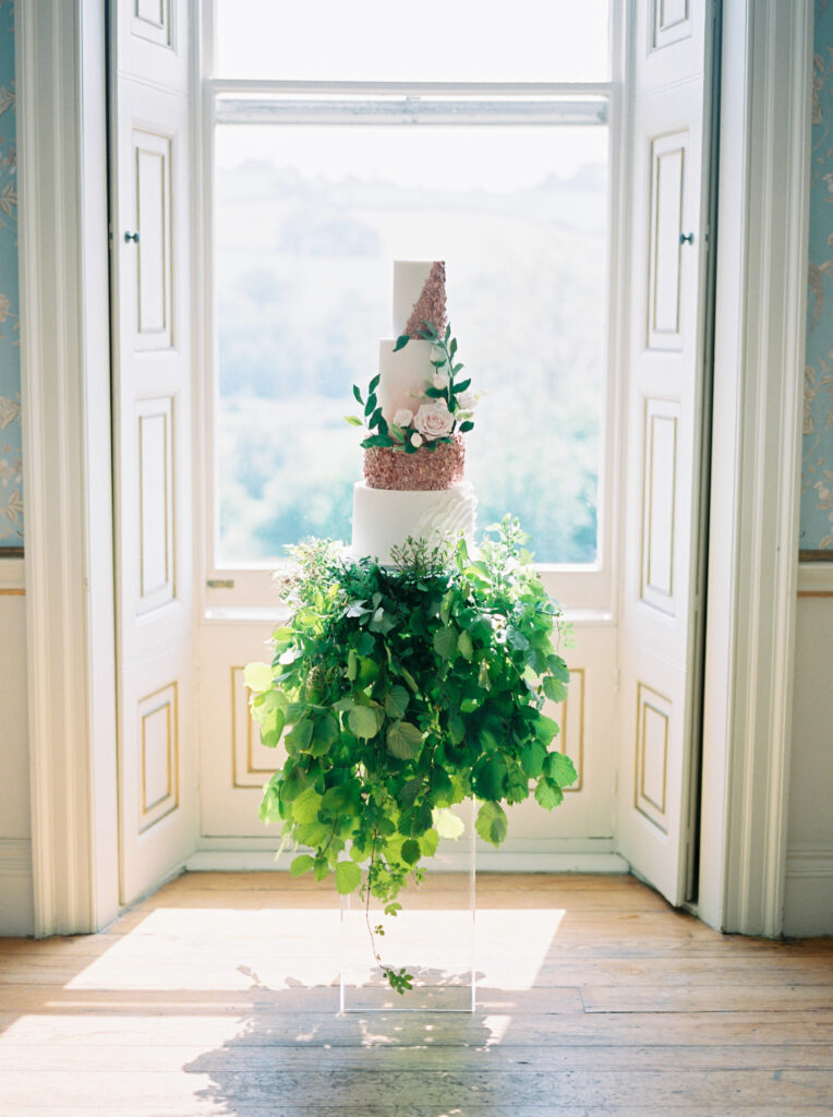Three tiered white and gold wedding cake, above foliage.