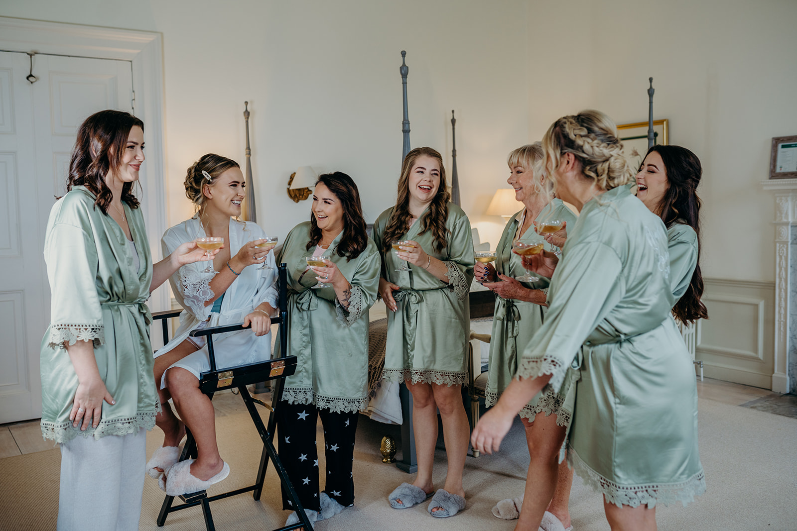 Bride laughing and standing with bridesmaids in bedroom.
