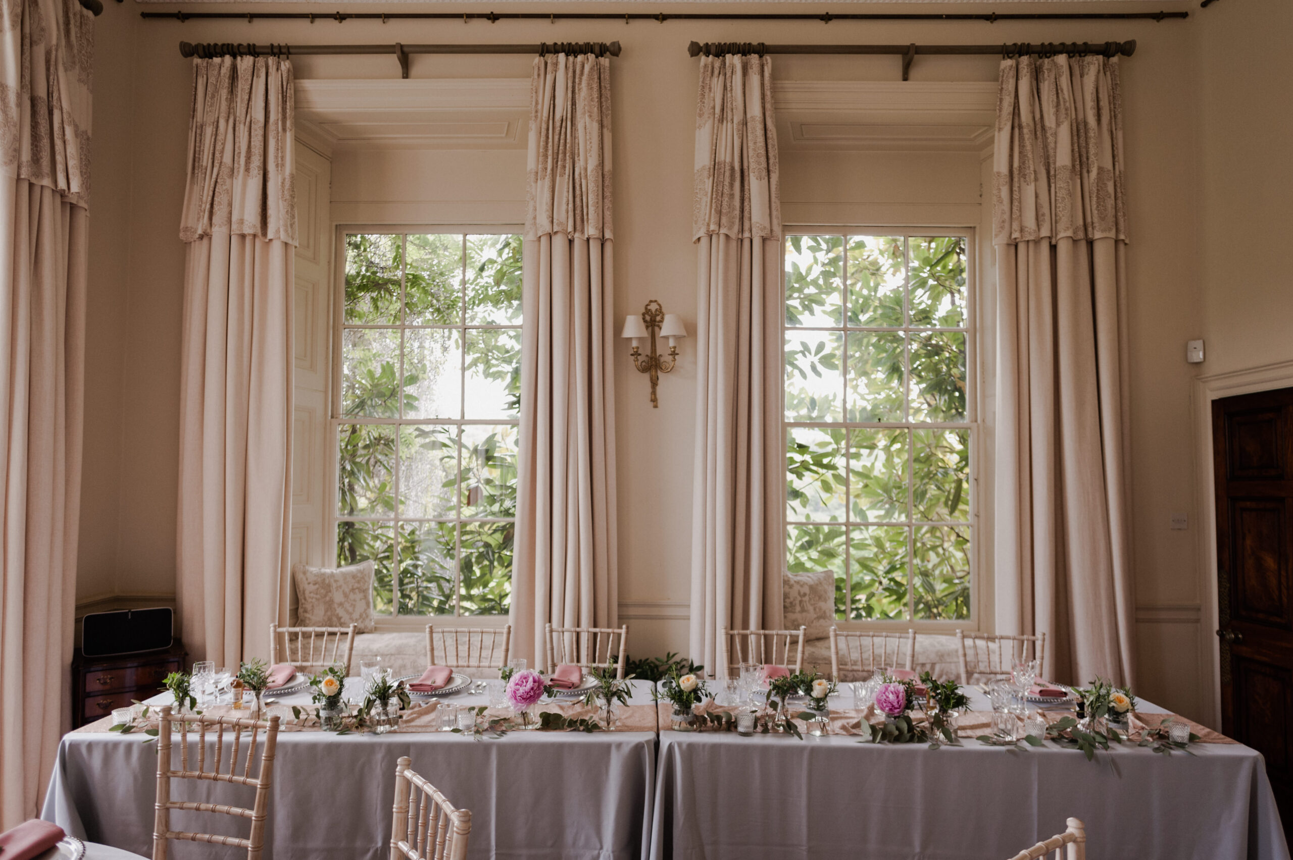 Wedding reception setup of long table in ballroom, by two windows.