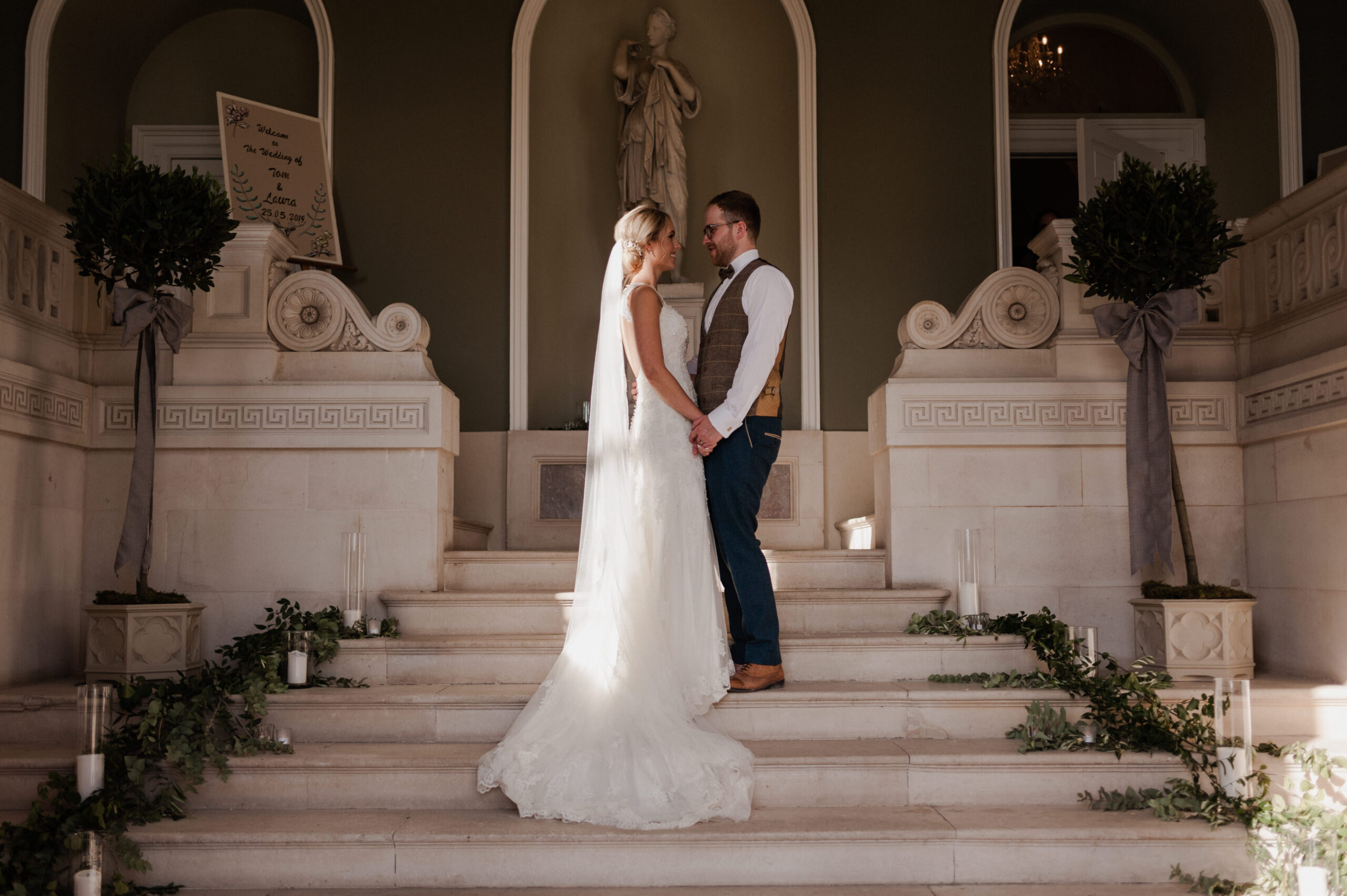 Bride and groom holding hands on stairs in entrance hall.