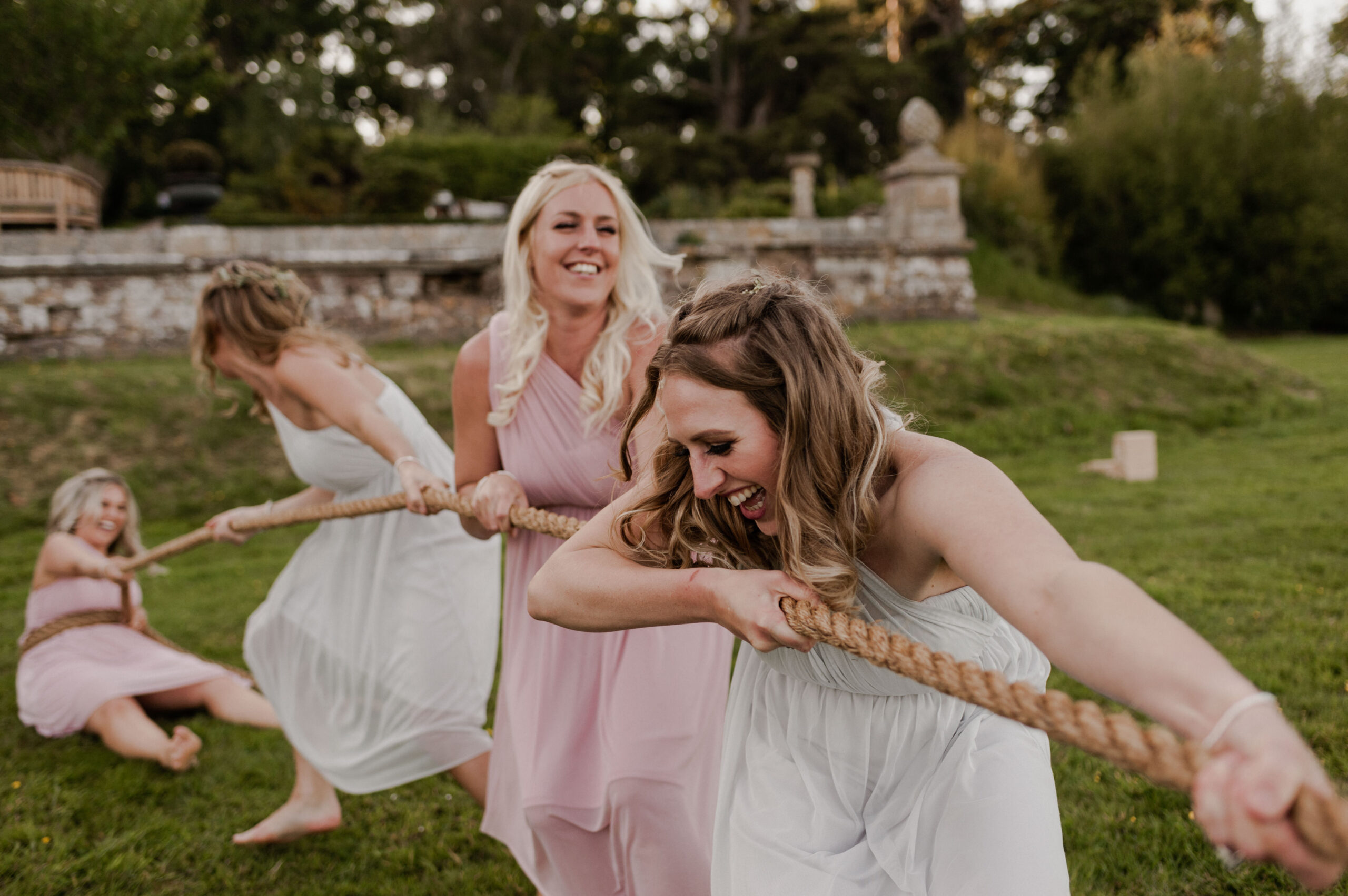 Bridesmaids playing tug of war on lawn.