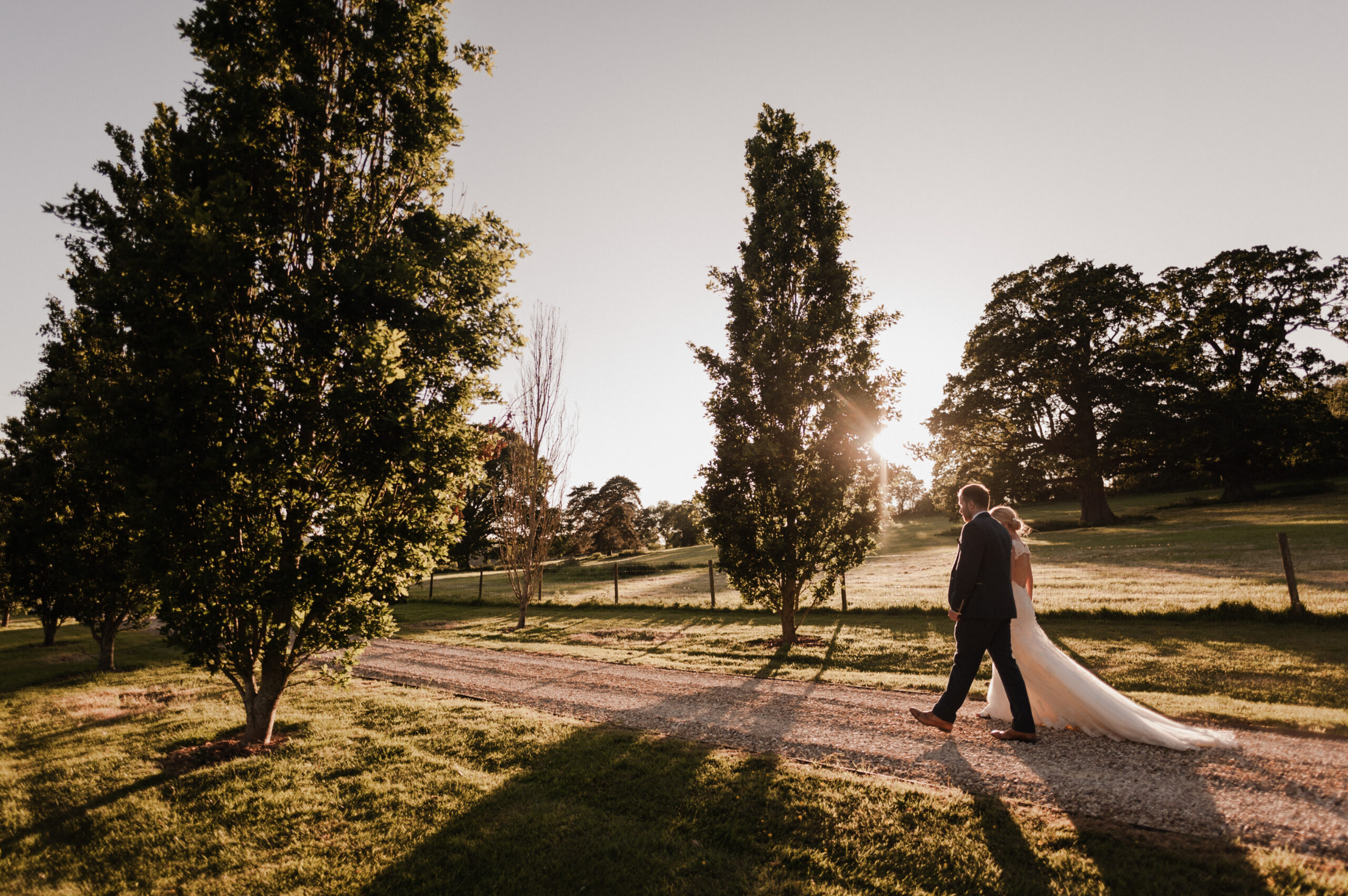 Bride and groom walking down tree lined driveway.