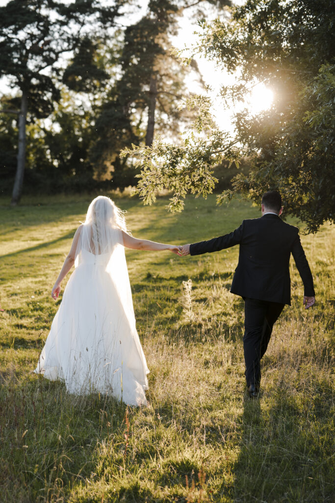 Bride and groom walking in an English field, holding hands.