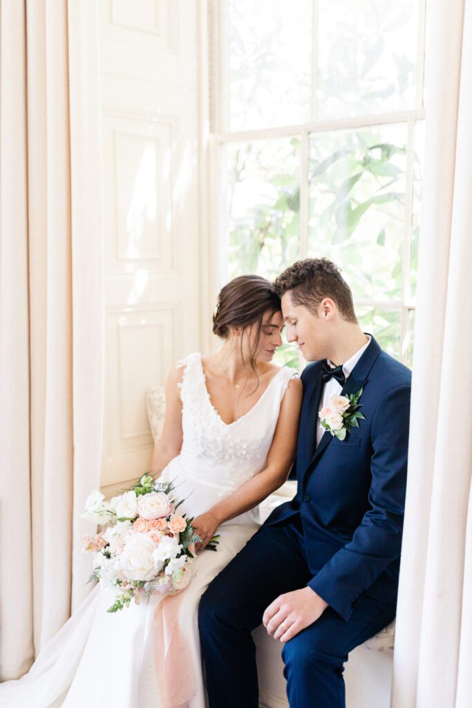 Bride and groom sitting by window in English country house.