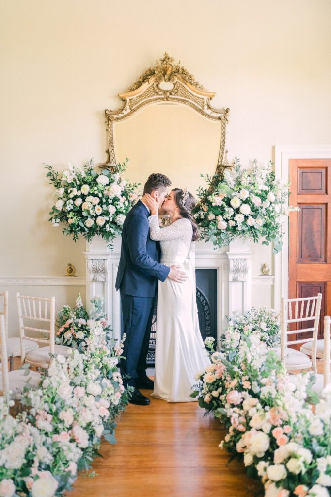 Bride and groom kissing at the altar, in English country house state room.