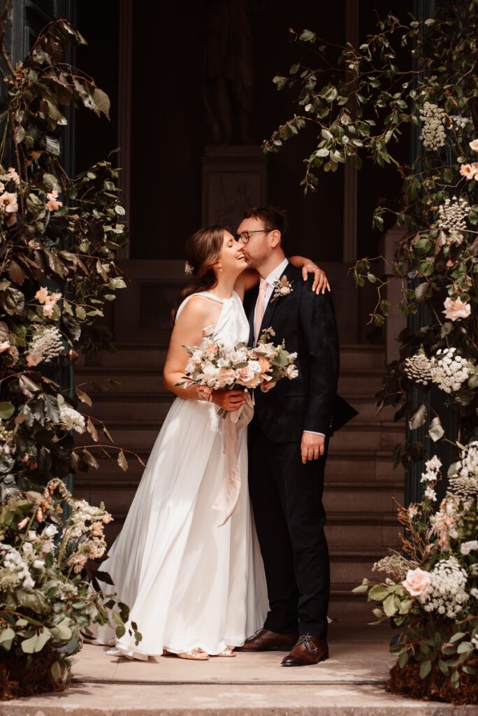 Bride and groom standing by luxurious floral arch.