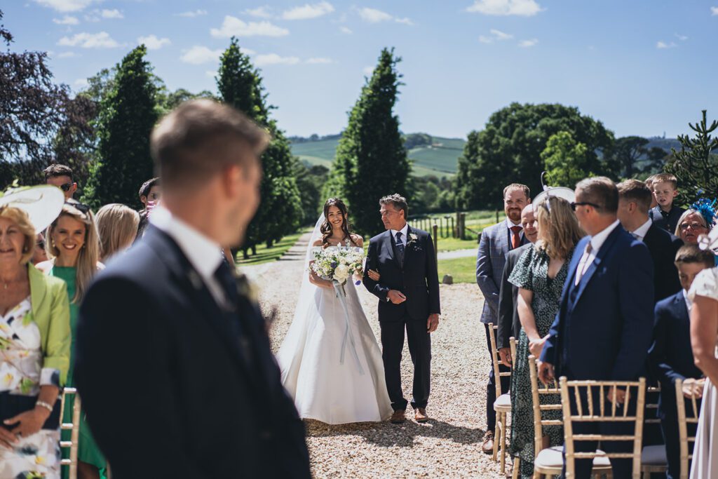 First look as bride walks down the aisle at outdoor wedding ceremony in the UK.