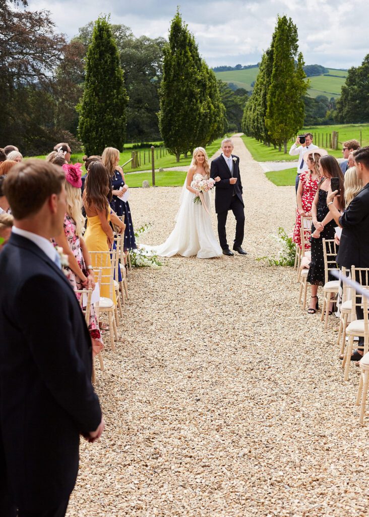 Bride and father of the bride walking down aisle at outdoor wedding ceremony.