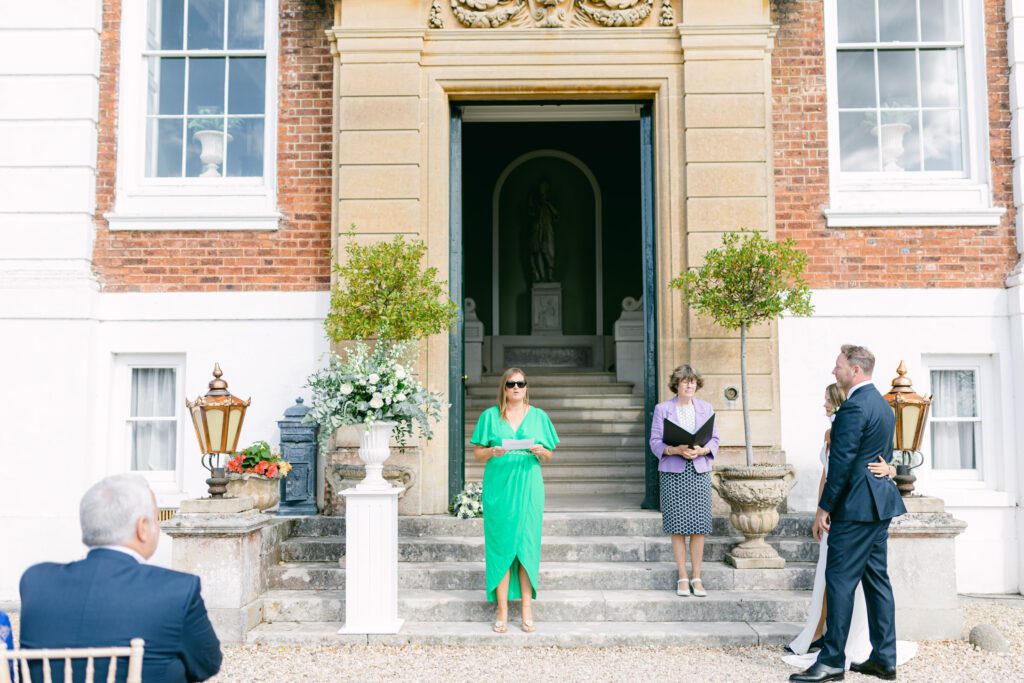 Wedding guest giving wedding reading, in front of English country house wedding venue.