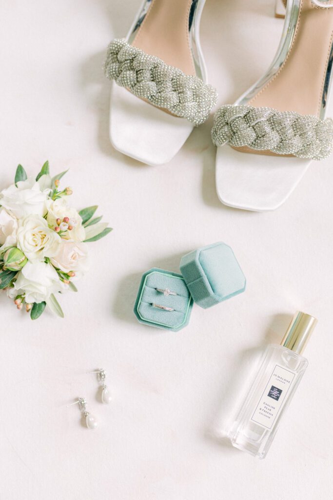 Flat lay of wedding rings, earrings, buttonhole and heels.