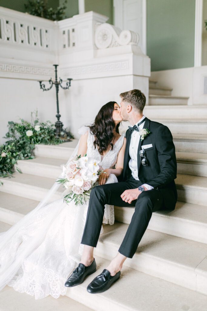 Bride and groom at black tie wedding, kissing on the steps in the entrance hall at a historical wedding venue.