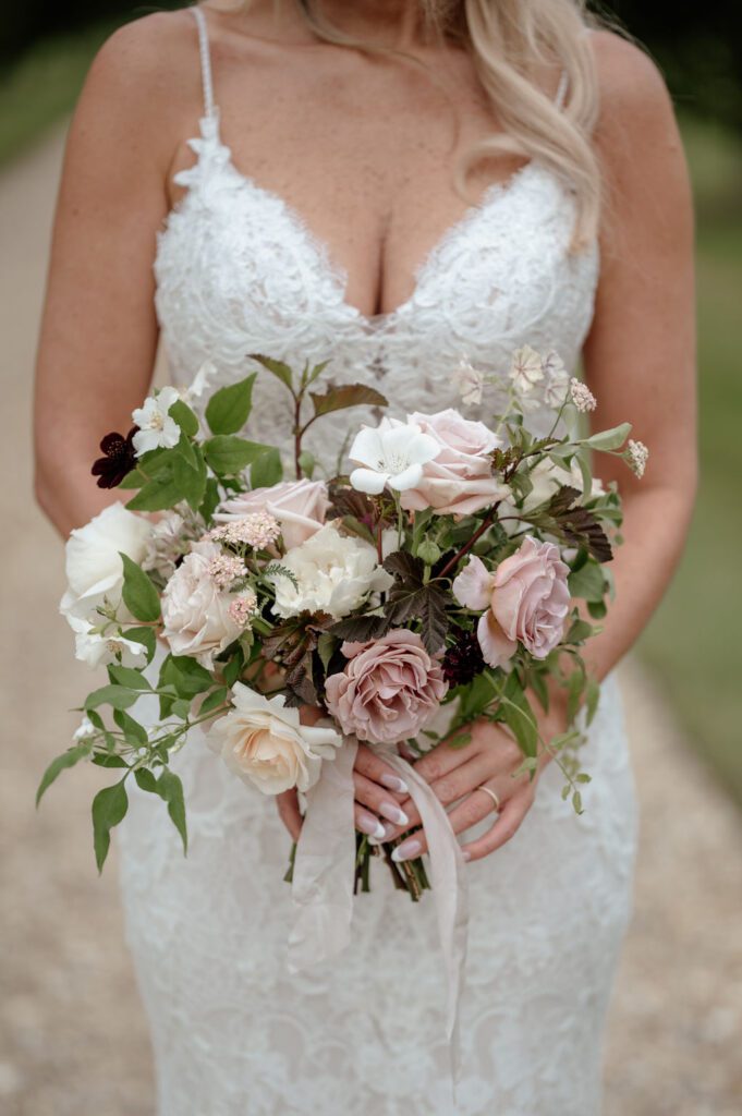 Bride holding bouquet of wedding flowers including roses and foliage, created by Miranda Hackett Flowers.