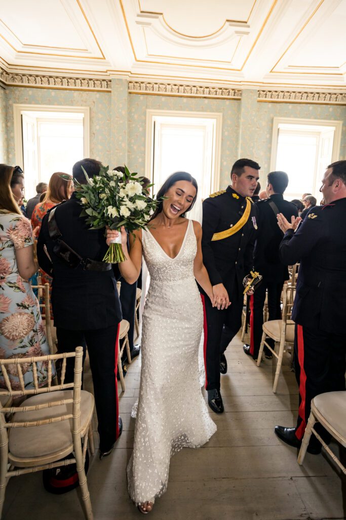 A bride and groom walk down the aisle at Pynes House, during their military themed wedding.