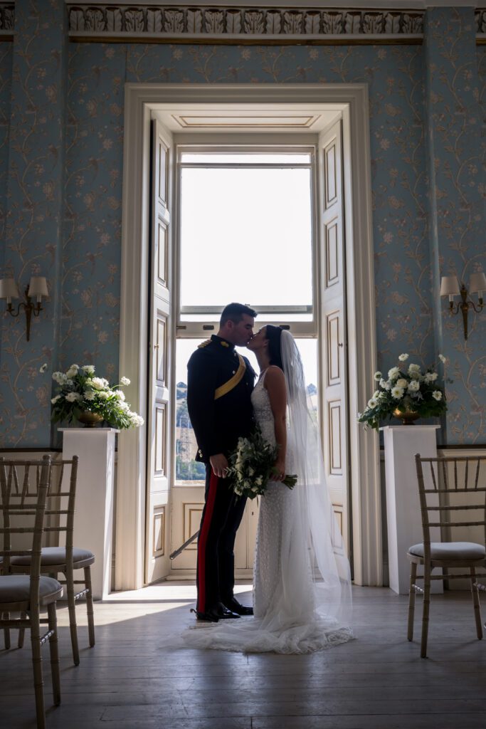 A bride and groom kiss at the top of the aisle, during a military wedding at an English country house.