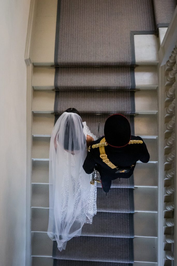 A bride and groom walk up the stairs of an English country house wedding venue, during their military inspired wedding.