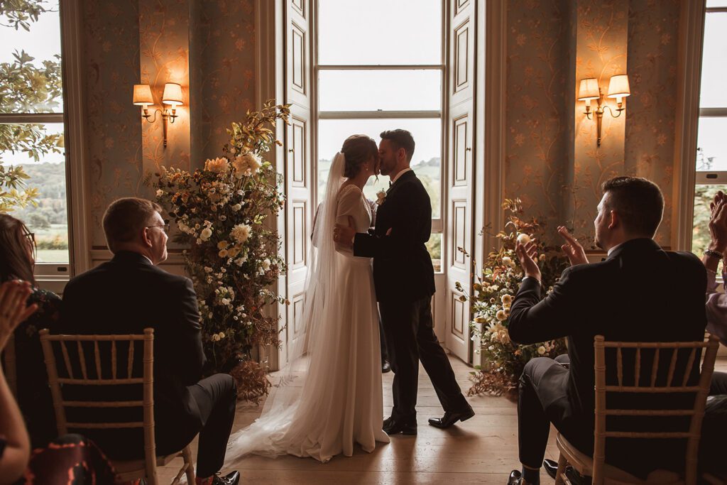 A bride and groom kiss at the altar, at a wedding in Devon.