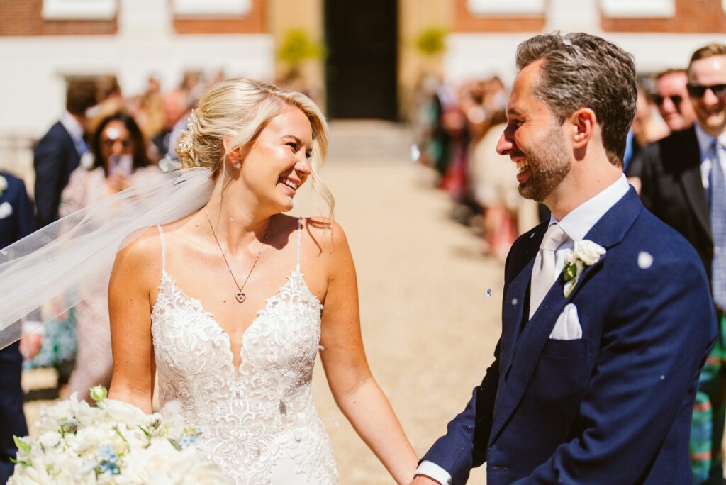 A bride and groom smile at each other, during a summer outdoor wedding.