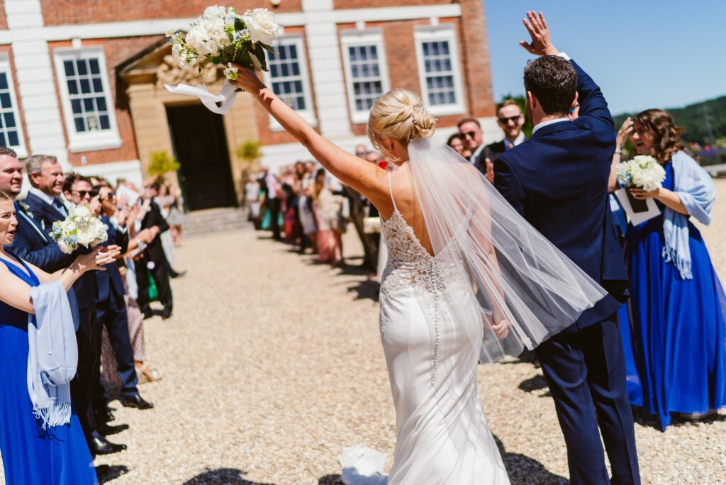 A bride and groom cheer with their guests, after a confetti shot for a Pynes House wedding.
