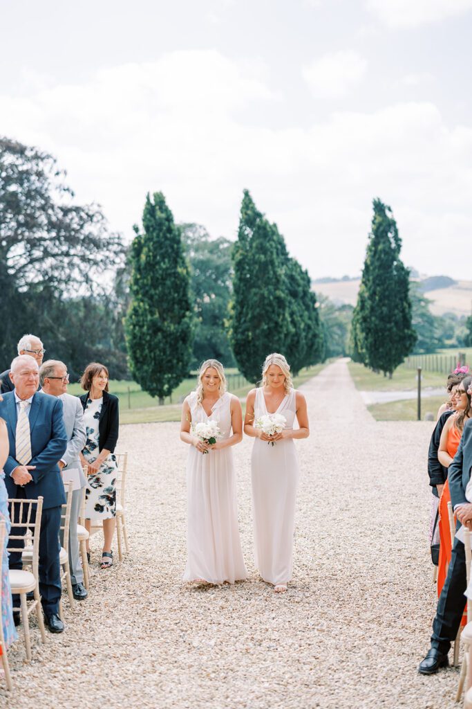The bridesmaids walk down the aisle at an outdoor wedding ceremony in Devon