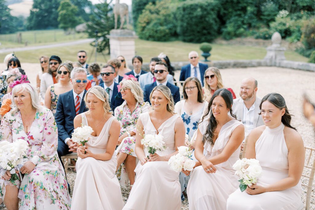 Bridesmaids smile at a wedding reading, during an outdoor ceremony