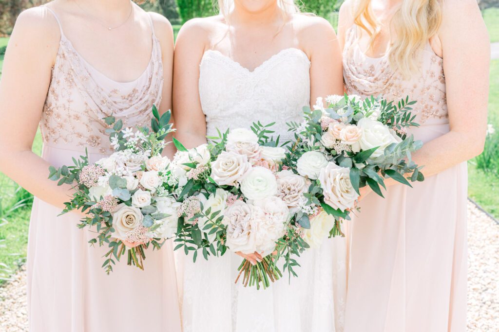 A bride and her bridesmaids hold their wedding bouquets together, during an English country garden wedding in the UK
