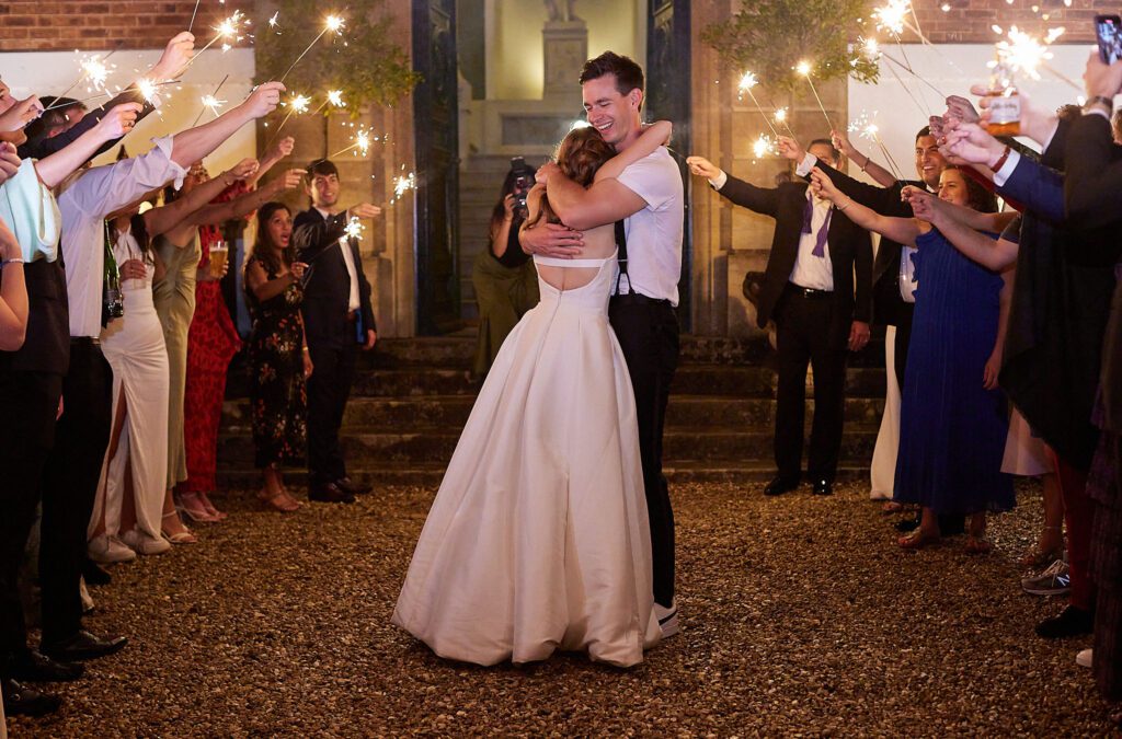 A tender moment as a bride and groom hug, during evening wedding sparklers