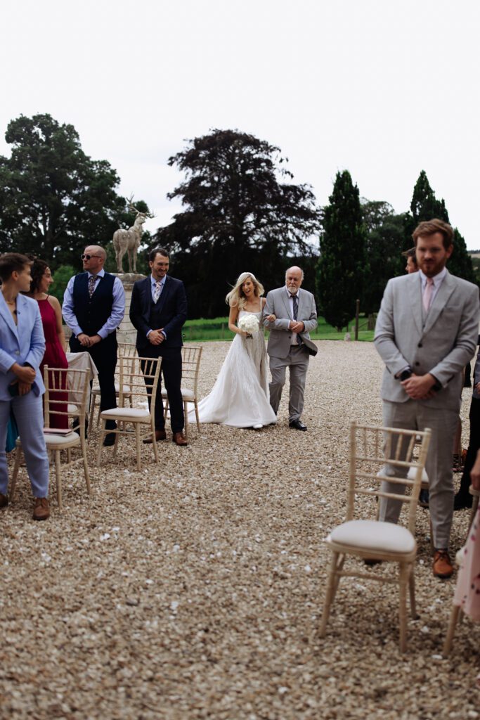 A bride and her father walk down the aisle during an outdoor wedding ceremony